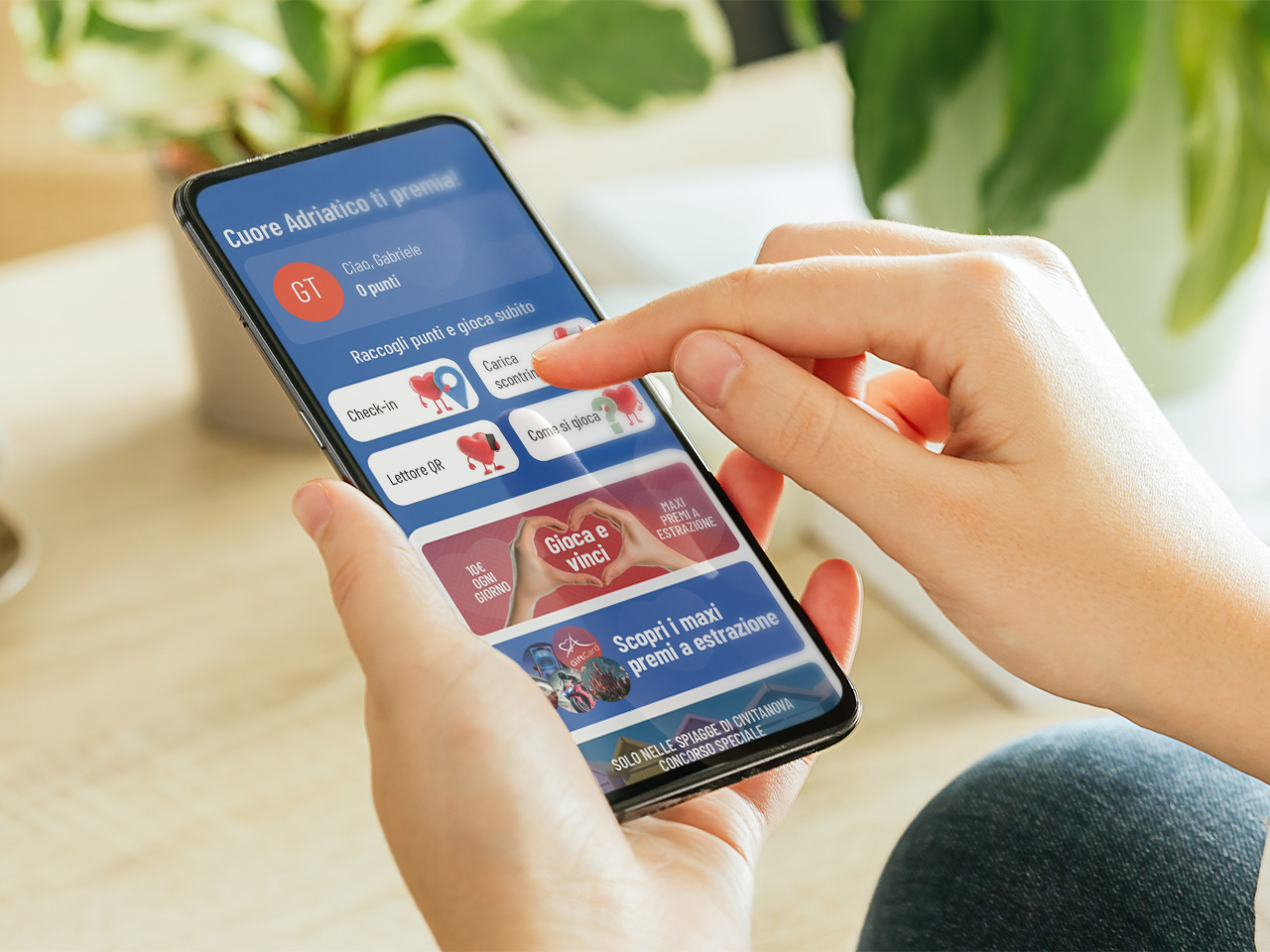 Una persona tiene in mano uno smartphone, interagendo con un'app di ricompense in italiano, con piante sullo sfondo.