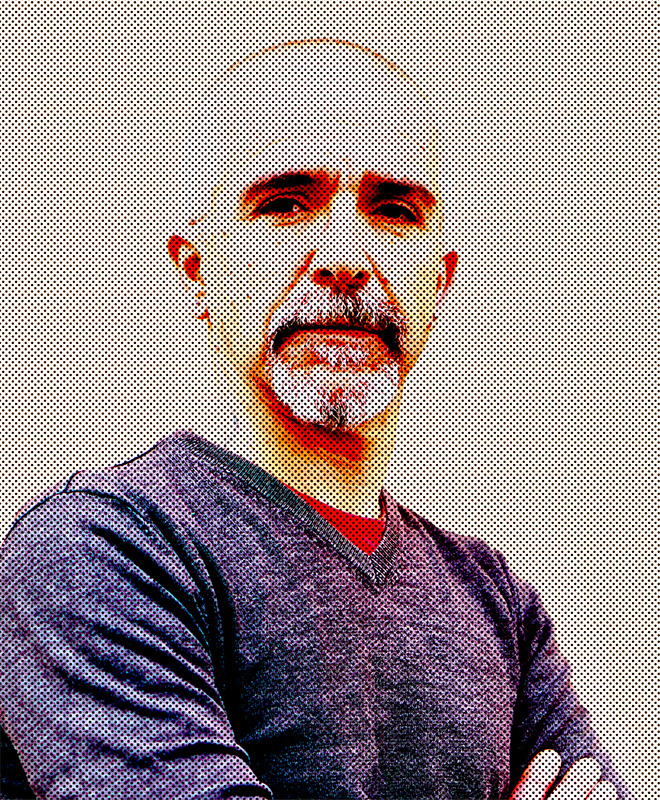 Un uomo con baffi e barba, con le braccia incrociate, in maglione scuro, con un effetto puntiforme stilizzato ad alto contrasto.