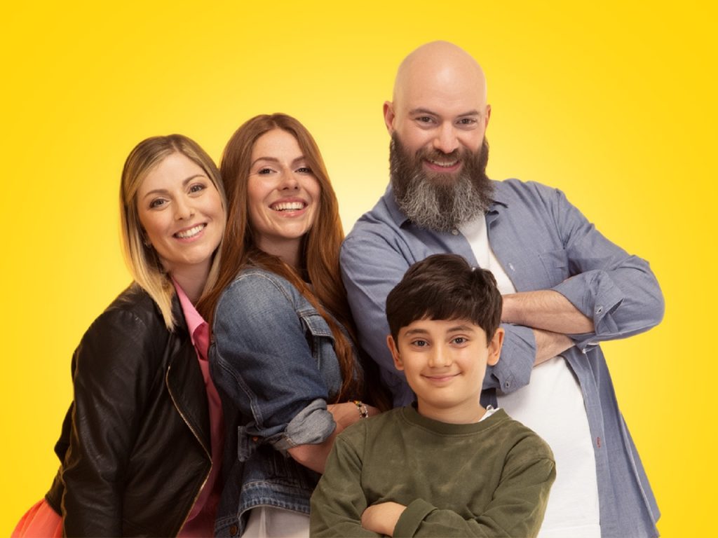 Four smiling people, including a child, pose together in front of a bright yellow background.