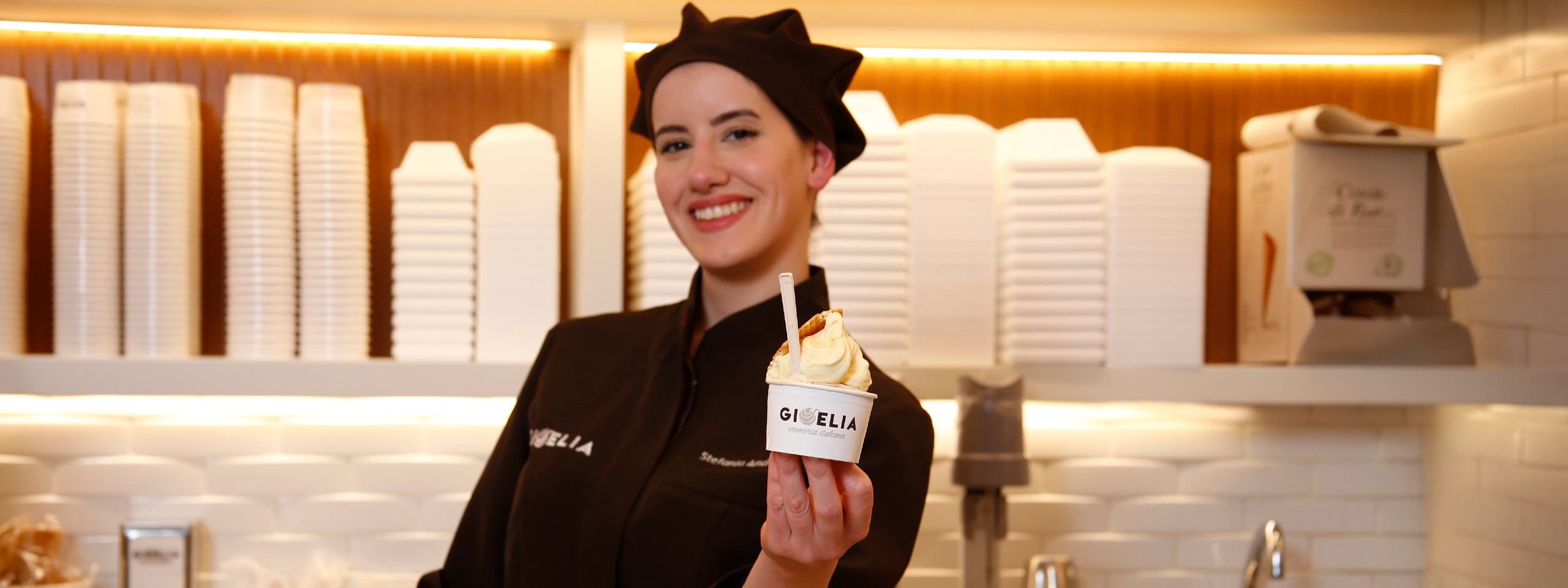 Lavoratore sorridente in uniforme tiene in mano una coppa di gelato in una gelateria.